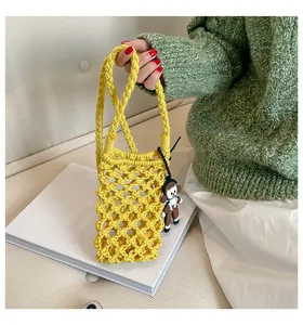 Close-up of yellow hollow crochet phone bag with a cute doll pendant detail