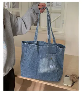 Dettaglio della borsa tote in denim a righe blu con tasca anteriore e logo cucito