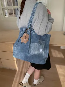 Borsa tote in denim a righe bianche e blu con ciondolo a forma di orso su una modella