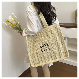 Detail of large straw beach tote bag with black LOVE LIFE embroidery and wide shoulder straps