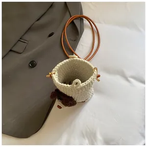 Detail van gehaakte puppy emmer tas met lederen riem op zacht minimalistisch bed