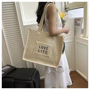 Detail of woven straw tote bag featuring black Love Life embroidery for beach vacation