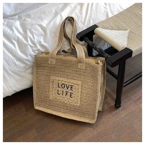 Detail of hand-woven straw beach tote with LOVE LIFE embroidery in a lifestyle setting
