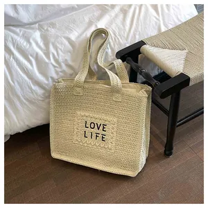 Detail of hand-woven straw tote bag texture featuring black Love Life stitched lettering