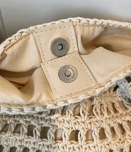 Detail van de metalen magneetsluiting en katoenen voering van de beige gevlochten tas