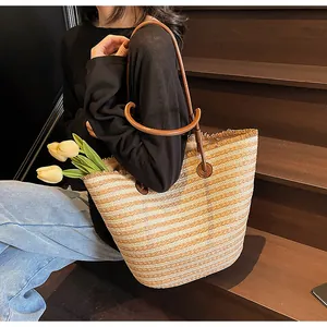 Detail of striped woven straw tote bag featuring leather straps and frayed fringe edges