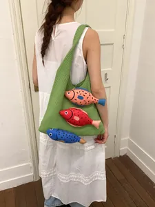 Sac cabas en tricot vert avec pendentifs poissons colorés porté par un mannequin