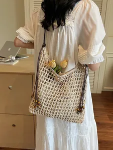 Hollow straw tote bag with wood bead strap shown on shoulder in a cozy home setting