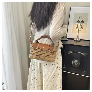 Detail of woven straw handbag with brown leather flap and gold clasp on a crossbody strap