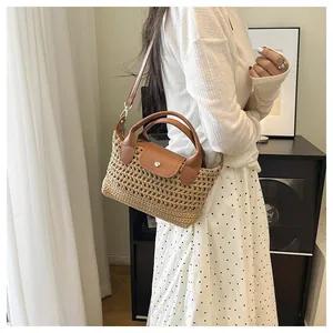Detail of woven straw handbag with brown leather handle and metal buckle on adjustable strap
