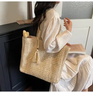 Détail d'un sac cabas en paille tressée avec pompons et perles en bois style bohème