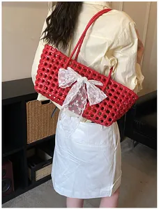 Détail d'un sac de plage tressé rouge orné d'un grand nœud en dentelle blanche avec anses
