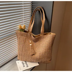 Détail d'un grand sac cabas en paille kaki avec un pompon décoratif et des perles