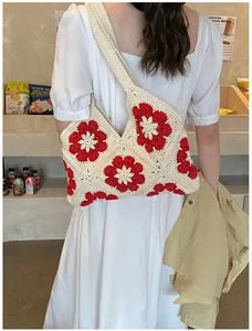 Close-up of handmade crochet shoulder bag with 3D red flowers on a white knit surface