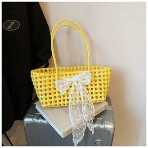 Détail d'un sac panier en tricot jaune évidé avec un grand nœud en dentelle blanche et anses