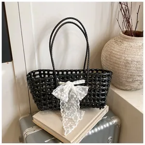 Détail du sac cabas tissé noir avec nœud en dentelle blanche sur livres et valise