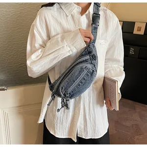 Detail of blue washed denim chest bag with multiple zipper compartments and nylon strap
