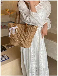 Detail of woven straw tote with leather strap and pearl lace bow on a white lace dress