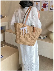 Close-up of woven straw tote bag with brown leather handles and delicate lace bow detail