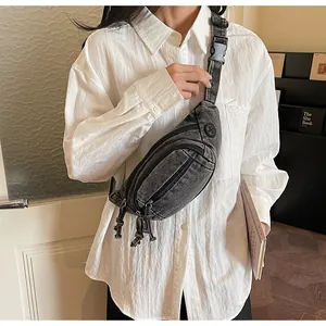 Detail of gray washed denim waist bag with multiple zippers and adjustable black strap