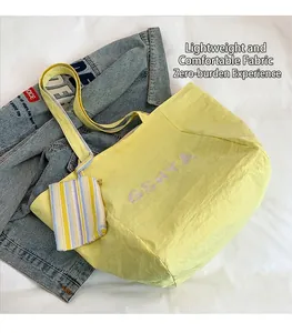 Detalle del bolso tote amarillo de tela ligera texturizada con colgante de rayas a juego
