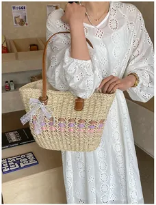 Detail showing woven straw tote with leather straps and delicate white lace bow accessory