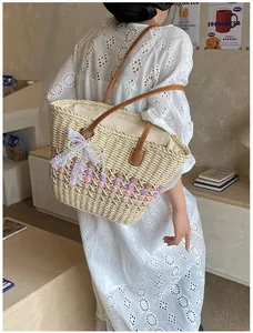 Detail of woven straw tote bag with pink wave pattern and brown leather handle