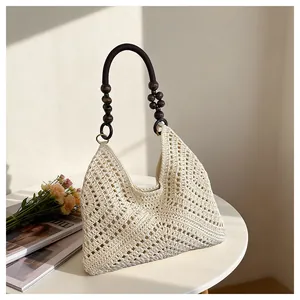Detail of hand-woven cream tote with decorative dark wood bead handles on white table