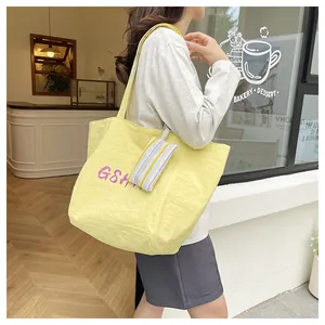 Detalle del bolso tote de nailon amarillo con letras moradas y un pequeño monedero