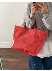 Macro shot of red glossy tote bag featuring intricate floral cutout details and handles