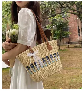 Detail of woven straw tote bag with brown leather straps and pearl tassel lace bow