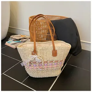 Detail of woven straw tote bag featuring brown leather handles and pearl lace bow charm