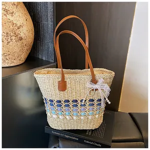 Detail of woven straw tote bag with gradient blue pattern, leather handles and pearl charm