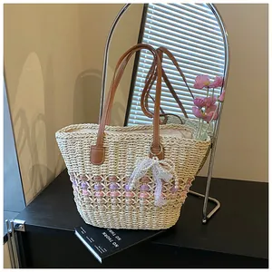 Detail of straw tote bag featuring contrast stripes, leather handles and bow charm
