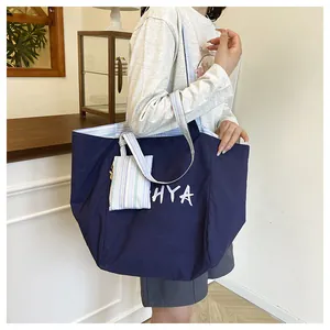 Detalle del bolso tote azul oscuro con logo HYA, correa a rayas y neceser a juego