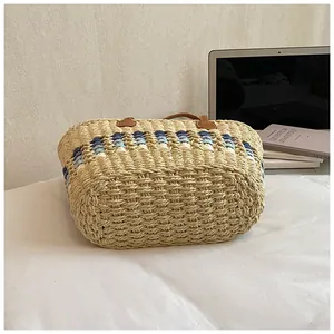 Detail of large straw tote bag with blue striped patterns and brown leather straps