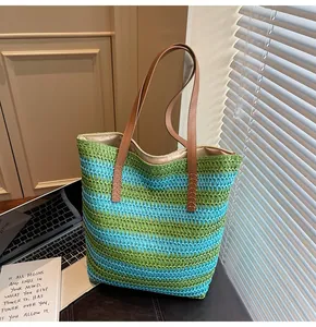 Detail of green and blue striped straw tote bag with brown leather shoulder straps