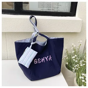 Detalle de bolso tote azul marino con mini estuche de rayas y bordado rosa frontal