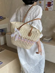 Woven straw tote bag with leather straps and lace bow detail on a fashion model