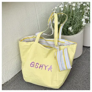 Vista detallada de bolsa tote amarilla con letras moradas e interior de rayas