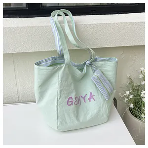 Detalle del bolso tote verde claro con correas de rayas moradas y mini colgante