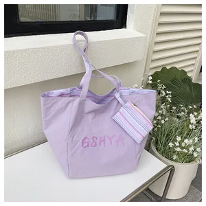 Detalle del bolso tote lavanda grande con logo GSHYA y pequeña bolsa de rayas en un banco blanco