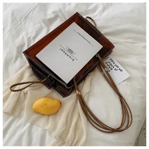 Detail shot of a brown transparent jelly tote bag with sleek leather handles on white fabric
