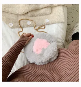 Detail of grey plush round bag featuring a pink heart and gold chain strap