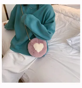 Detail of pink plush round crossbody bag featuring a white heart and gold chain strap