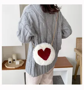 Detail of round plush crossbody bag with red heart and gold chain strap on grey sweater