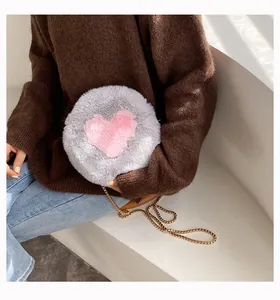 Detail of grey plush round bag featuring a pink heart and elegant gold chain strap