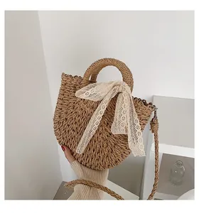 Detailed close-up of straw woven crossbody bag with cream lace bow and long strap
