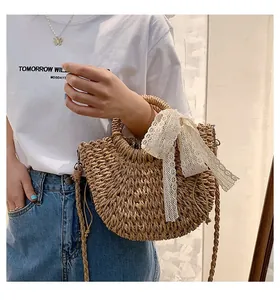 Detail of straw half-moon handbag featuring a large white lace bow and woven shoulder strap