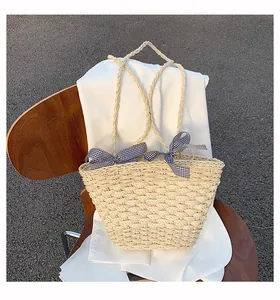 Dettaglio borsa in paglia intrecciata beige con fiocchi in nastro a quadretti bianchi e neri